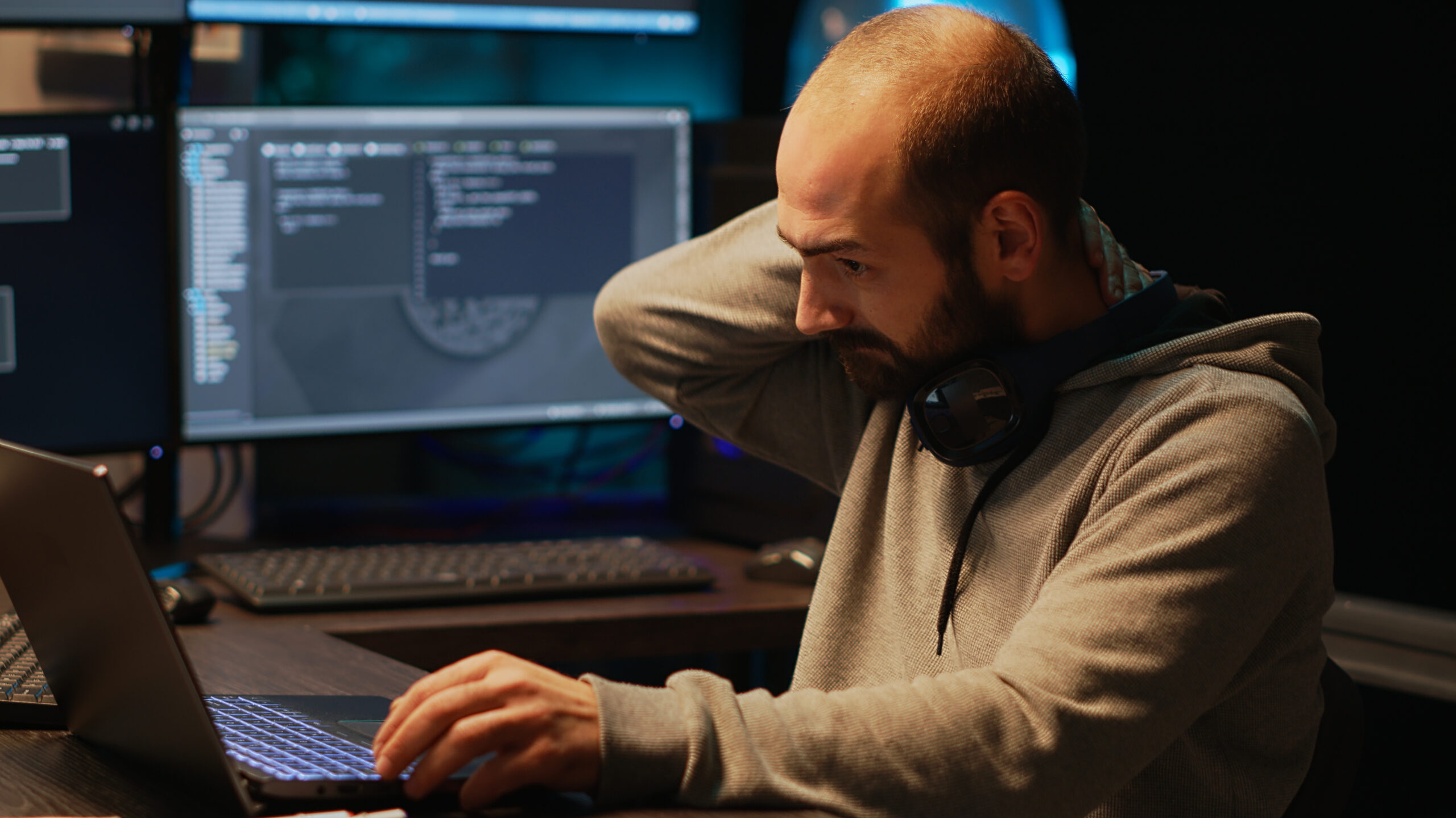 Male in casual clothes sitting at technical furniture rubbing his neck from strain.